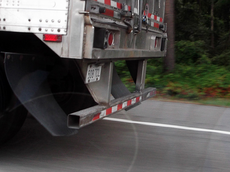 Photo of the rear of a truck from the side, showing the metal bars that form the underride guard at the back of the truck.
